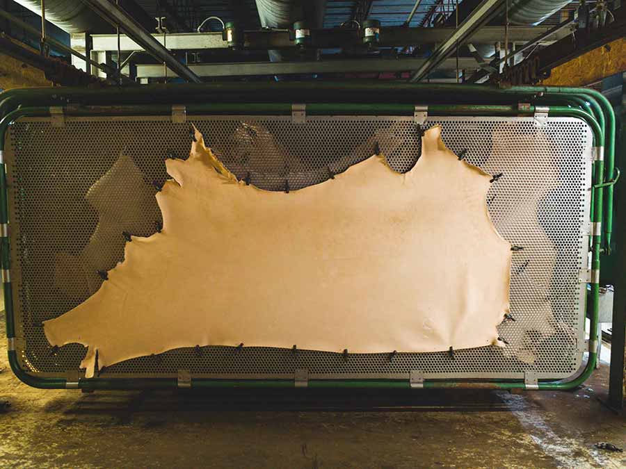 Large hide stretched on metal frame in industrial workshop, showcasing American leather craftsmanship.