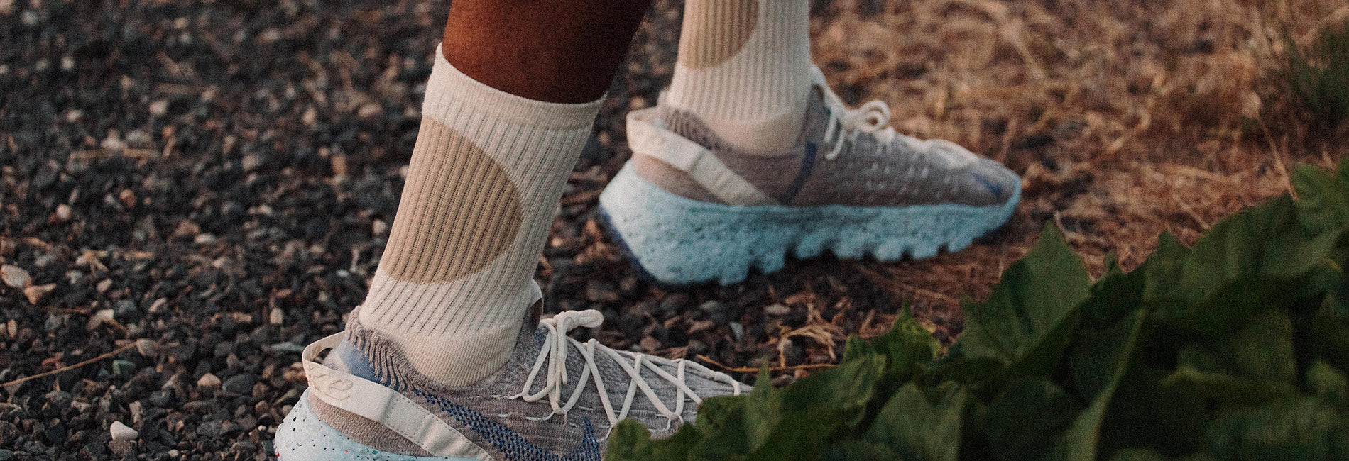Cream and beige geometric-patterned socks paired with stylish sneakers on a gravel path, evoking outdoor adventure and modern comfort.