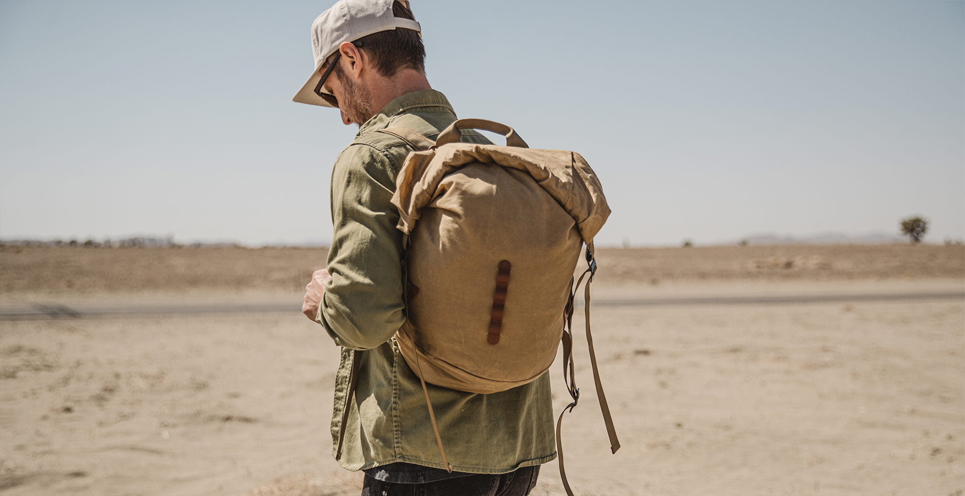 Man in desert with tan backpack and olive shirt, embodying rugged adventure style.
