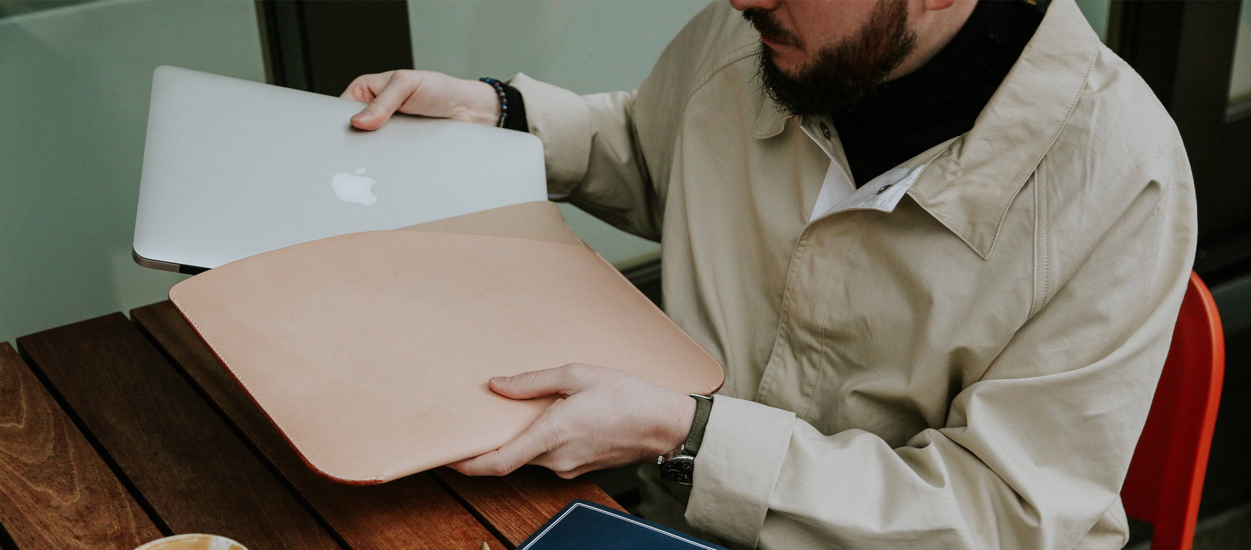 Man placing MacBook into tan leather sleeve, minimalist tech lifestyle, premium accessories.