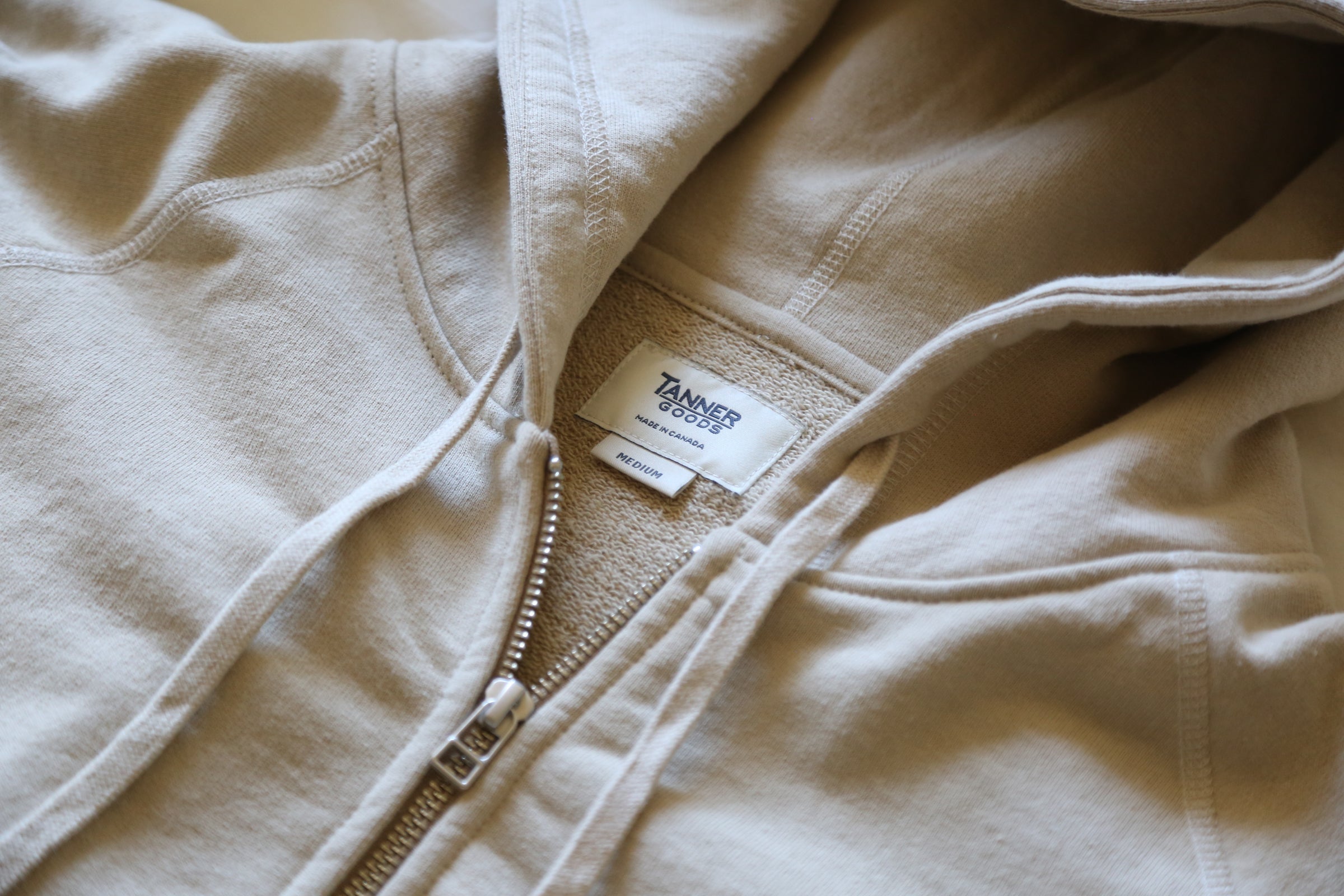 Soft beige zip hoodie with Tanner Goods label, cozy texture, minimalist design, Canadian-made comfort.