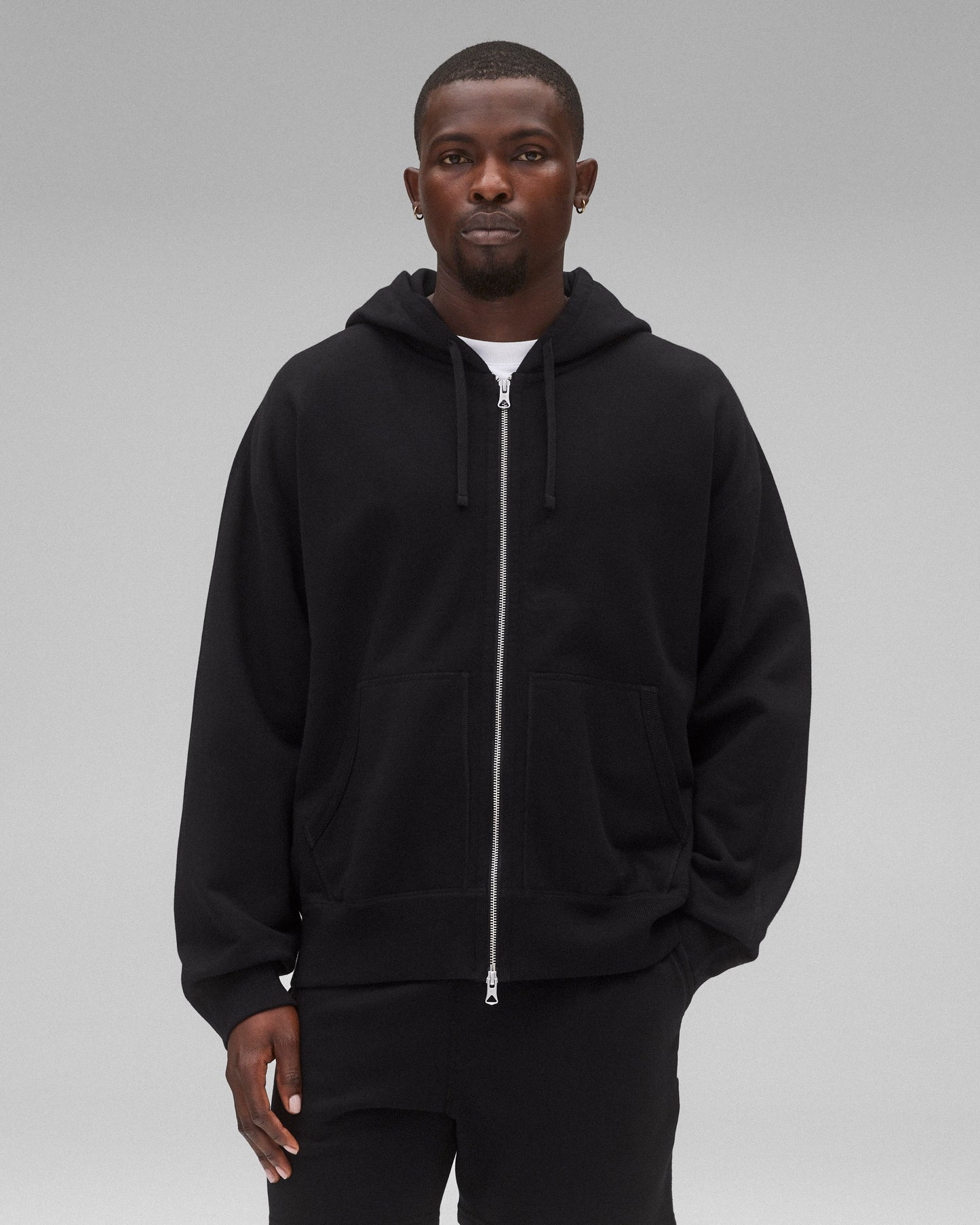 Black Midweight Terry Relaxed Zip Hoodie with silver zipper and front pockets, worn by a man.