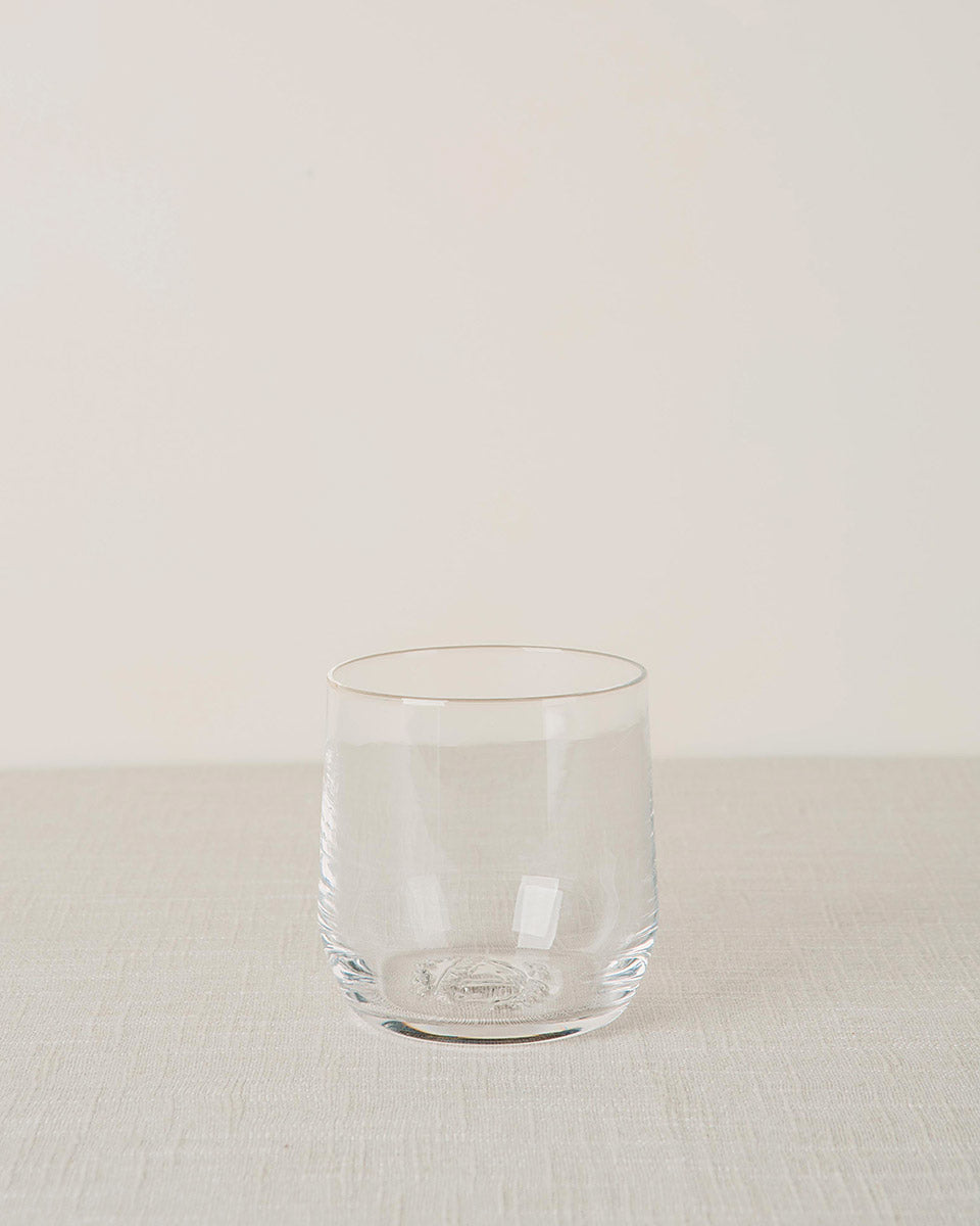 Clear stemless cocktail glass with subtle vertical ridges and an embossed base, on a light textured fabric.