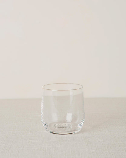 Clear stemless cocktail glass with subtle vertical ridges and an embossed base, on a light textured fabric.