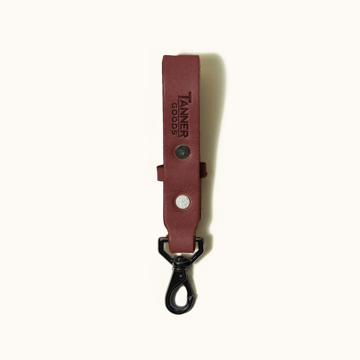 Cognac leather key lanyard by Tanner Goods, with a black metal swivel clip and silver-toned rivets, on a white background.