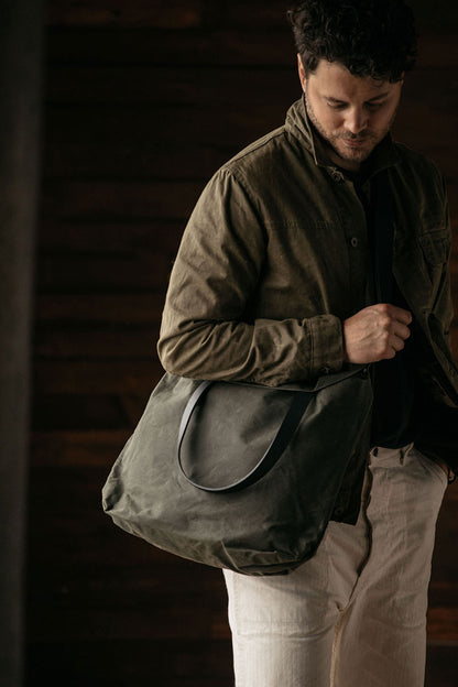 Juniper Green waxed canvas simple tote bag held by a man wearing an olive jacket and light pants.