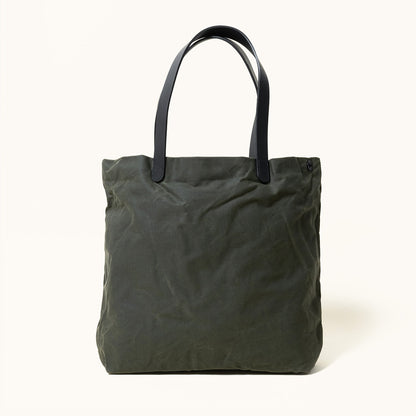 Juniper green waxed canvas tote bag with black leather handles and subtle fabric wrinkles, front view.