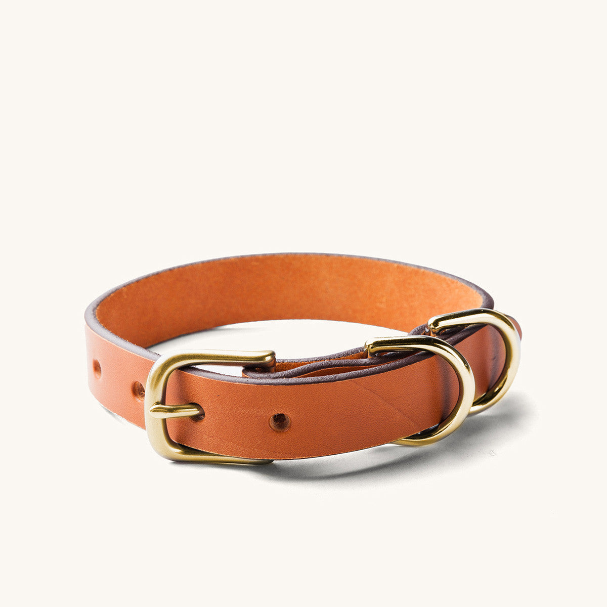 Saddle tan leather dog collar with a brass buckle and two D-rings on a white background.