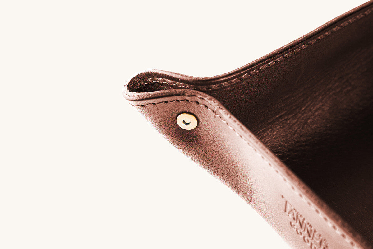 Cognac leather valet tray with a brass snap button, detailed stitching, and embossed text on the side.